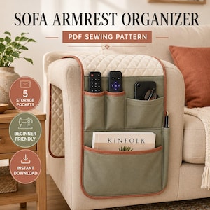 May include: A sofa armrest organizer PDF sewing pattern featuring a quilted cream top section and olive green fabric pockets. The organizer includes five storage pockets holding two remote controls, a smartphone, a pen, and a book titled KINFOLK.