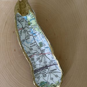 May include: An oyster shell with a gold-painted exterior and a decoupage interior featuring a map of North Carolina and South Carolina, including towns like New London, Norwood, Ansonville, Wadesboro, and Chesterfield with visible road routes.