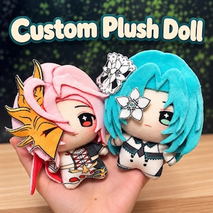 Puede incluir: Dos muñecos de peluche personalizados con diseños estilo anime. Uno tiene cabello rosa con un accesorio amarillo en forma de llama, mientras que el otro tiene cabello verde azulado con una flor blanca. Ambos tienen rostros bordados y trajes detallados.