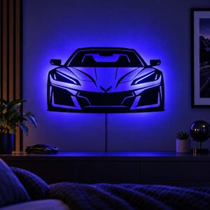 May include: A wall-mounted LED light fixture shaped like the front silhouette of a sports car. The black metal frame features sharp, angular lines and a central emblem, illuminated from behind by a vibrant blue glow that casts light onto the wall.