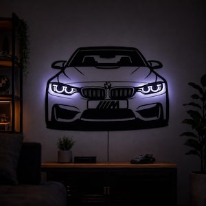 Könnte beinhalten: Ein Wandkunstobjekt aus schwarzem Metall in Form der Front eines BMW M-Autos mit integrierter weißer LED-Hintergrundbeleuchtung, die die Scheinwerfer und die Konturen des Autos hervorhebt. Das Design zeigt das BMW-Logo und ein M-Emblem.