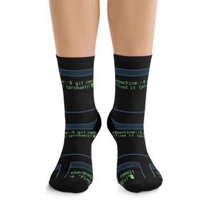 May include: A pair of black crew socks featuring a repeating pattern of blue terminal window frames and green command line text that reads user@machine:~$ git commit -m "fixed it (probably)" with a blinking cursor block at the end of the text.
