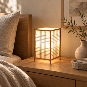 May include: A rectangular table lamp featuring a light-colored wooden frame with a grid pattern and a translucent white shade that emits a warm, soft glow. The lamp stands on a flat surface, showcasing its structured design and clean lines.
