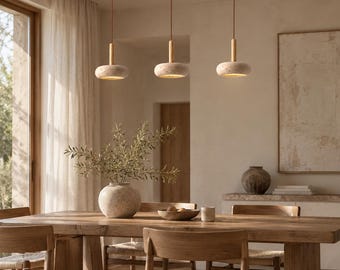 May include: A linear pendant light fixture featuring three circular, textured stone-like shades suspended from a dark rectangular ceiling mount by thin cords. Each shade includes a light-colored wooden cylindrical connector at the top.