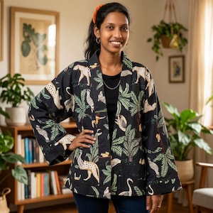 Può includere: Giacca kimono nera con stampa giungla, con leopardi e piante tropicali. La giacca ha una vestibilità ampia e maniche larghe. La giacca è indossata sopra un top nero. Il design ricorda un paradiso tropicale.