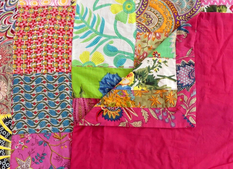 K&ouml;nnte beinhalten: Eine Patchwork-Decke mit rosa R&uuml;ckseite und einem bunten Patchwork-Design mit Blumenmustern, geometrischen Formen und Paisley-Drucken.