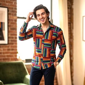 Peut inclure: Une chemise à manches longues avec un motif patchwork coloré. La chemise présente un mélange vibrant de motifs rectangulaires rouges, bleus, verts, jaunes et oranges. La chemise est associée à un pantalon bleu foncé.
