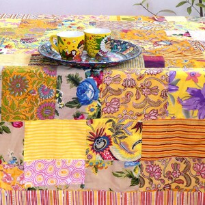 Peut inclure: Une nappe de patchwork jaune avec une vari&eacute;t&eacute; de motifs floraux et g&eacute;om&eacute;triques. Deux tasses en c&eacute;ramique jaunes avec des motifs color&eacute;s sont sur une assiette &agrave; motifs bleus et blancs.