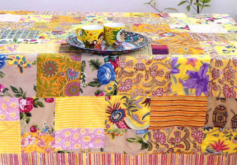 Peut inclure: Une nappe de patchwork jaune avec une vari&eacute;t&eacute; de motifs floraux et g&eacute;om&eacute;triques. Deux tasses en c&eacute;ramique jaunes avec des motifs color&eacute;s sont sur une assiette &agrave; motifs bleus et blancs.