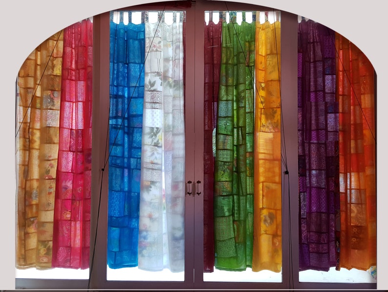 May include: A set of eight sheer curtains in various colors, including orange, red, blue, white, green, yellow, purple, and orange. The curtains are made of a patchwork of fabric squares and are hung on a window.