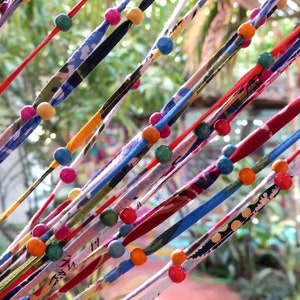 May include: A colorful string curtain with wooden beads in various colors, including red, blue, green, yellow, and orange. The curtain is made of fabric strips with different patterns and textures.