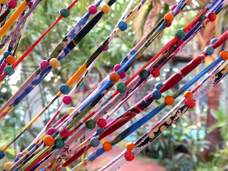 May include: A colorful string curtain with wooden beads in various colors, including red, blue, green, yellow, and orange. The curtain is made of fabric strips with different patterns and textures.