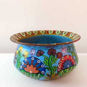 May include: A hand-painted ceramic bowl with a blue glaze and floral designs in shades of red, green, yellow, and blue. The bowl has a wide rim with a decorative pattern.