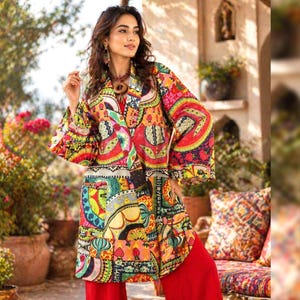 May include: A vibrant, patterned coat with a mix of red, yellow, green, and blue colors. The coat has a unique design and is paired with red pants. The overall style is bohemian and artistic.