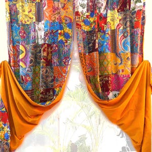 May include: Two patchwork curtains with vibrant colors and patterns, including floral and paisley designs. The curtains are held back with bright orange fabric, creating a layered effect. The curtains are hanging in front of a window.