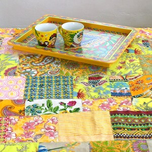 Peut inclure: Un plateau jaune avec un motif floral color&eacute; et un bord festonn&eacute;. Deux tasses en c&eacute;ramique jaunes avec des motifs color&eacute;s sont sur le plateau. Le plateau est sur une courtepointe en patchwork avec une vari&eacute;t&eacute; de tissus color&eacute;s.