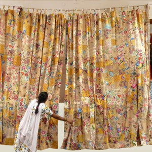 Può includere: Un set di tende colorate realizzate in tessuto patchwork. Le tende sono un mix di giallo, arancione, marrone e bianco con motivi floreali. Le tende sono appese a una parete bianca.