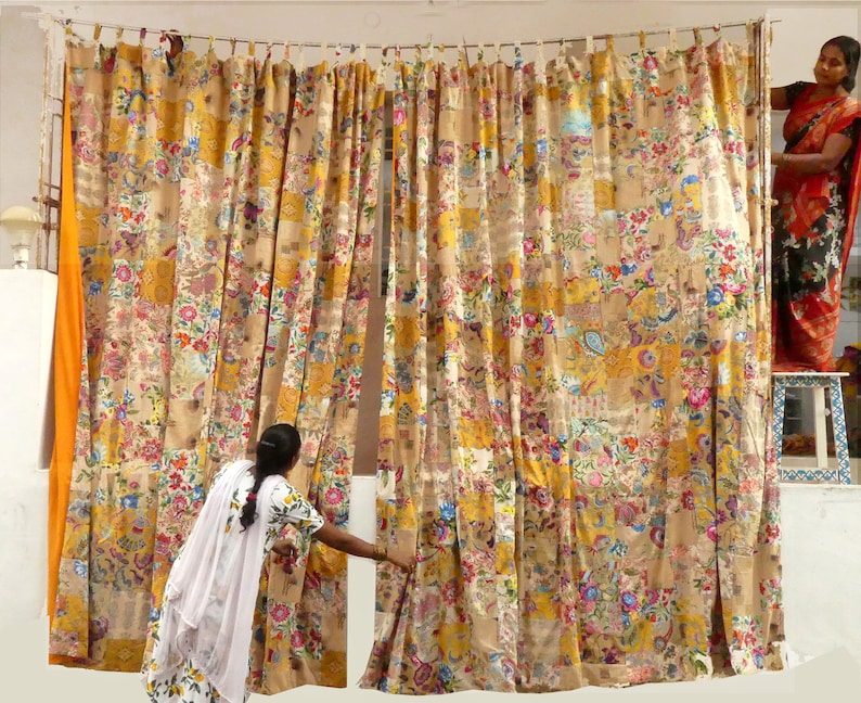 May include: A set of colorful curtains made from patchwork fabric. The curtains are a mix of yellow, orange, brown, and white with floral patterns. The curtains are hung on a white wall.