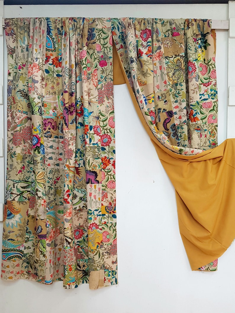 May include: A pair of curtains with a patchwork design featuring a variety of floral patterns in shades of pink, blue, green, and yellow. The curtains are made of a lightweight fabric and have a subtle sheen. The curtains are hung on a white rod and are pulled back to reveal a yellow fabric behind them.