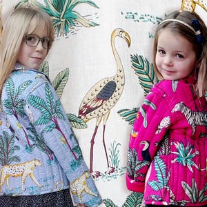 May include: Two girls wearing colorful jackets with tropical print designs. The jackets feature a variety of animals and plants, including flamingos, toucans, zebras, and palm trees. The girl on the left is wearing a light blue jacket, while the girl on the right is wearing a pink jacket.