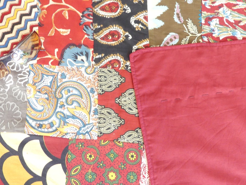 Peut inclure: Une courtepointe en patchwork avec divers tissus color&eacute;s, notamment rouge, bleu, jaune et vert. La courtepointe est compos&eacute;e de diff&eacute;rents motifs, notamment des motifs paisley, floraux et g&eacute;om&eacute;triques. La courtepointe est cousue avec du fil rouge.