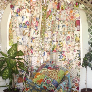 May include: A patchwork curtain made of colorful fabric squares with floral and paisley patterns. The curtain is hung in a window with a white frame and a white lattice design. A potted plant sits in front of the curtain.