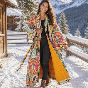 May include: A long, colorful patterned robe with a yellow lining. The robe features a vibrant mix of red, blue, green, and yellow patterns. The person is wearing black pants and brown boots, standing in a snowy outdoor setting.