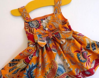 Little girl dress in orange cotton, large paisley print, with red trim and braid