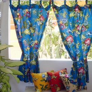 以下が含まれることがあります： 青い花柄のカーテンと、お揃いのクッション。カーテンは赤、黄、青の花の鮮やかな模様です。クッションは黄色、赤、青の花柄です。カーテンはシンプルなロープでまとめられています。