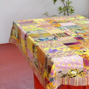 Peut inclure: Une nappe patchwork avec un motif jaune, orange, rose et violet. La nappe est faite de diff&eacute;rents tissus et motifs, cr&eacute;ant un design unique et color&eacute;.