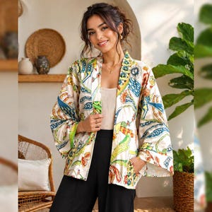 K&ouml;nnte beinhalten: Eine cremefarbene Kimono-Jacke mit einem farbenfrohen, gemusterten Design mit blauen, gelben und roten Akzenten. Die Jacke hat weite &Auml;rmel und ist vorne offen. Das Model tr&auml;gt eine schwarze Hose und ein cremefarbenes Oberteil.