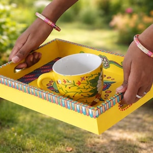Peut inclure: Un plateau de service jaune avec un motif floral et une tasse à thé jaune assortie. Le plateau a une bordure colorée et est tenu par deux mains. La tasse à thé a un intérieur blanc et une anse jaune.