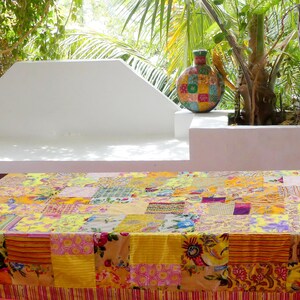 Peut inclure: Une nappe de patchwork color&eacute;e avec des carr&eacute;s jaunes, roses et orange, pos&eacute;e sur une table blanche avec un vase d&eacute;coratif en arri&egrave;re-plan.