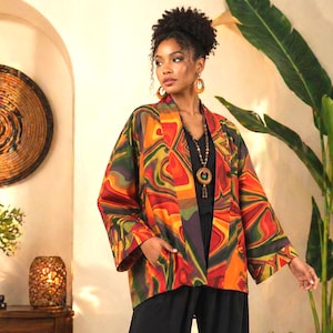 Könnte beinhalten: Ein lebendiger, gemusterter Kimono in Rot-, Orange-, Grün- und Gelbtönen. Die Jacke mit offenem Schnitt hat ein einzigartiges, abstraktes Design. Das Model trägt ein schwarzes Oberteil und eine Hose sowie eine lange Halskette.