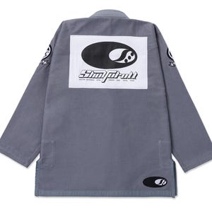May include: A grey long-sleeve gi jacket featuring a large white rectangular patch on the back with a black oval logo and the text "Simp-roll" above a list of cities. Smaller circular logos are present on the sleeves and the lower front hem.