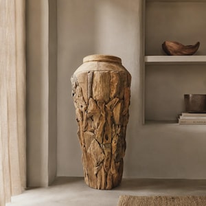 Könnte beinhalten: Eine hohe Bodenvase, die aus zahlreichen unregelmäßigen Stücken hellbraunem Teakholz gefertigt ist. Das Gefäß hat einen zylindrischen Körper mit einer strukturierten, mosaikartigen Oberfläche aus Holzfragmenten und einen glatten, flachen Rand.