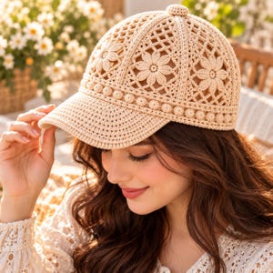 Puede incluir: Una gorra de béisbol de ganchillo en color beige con un patrón floral detallado en la copa, un pequeño botón circular en la parte superior y una hilera de pequeñas cuentas esféricas en la base. La visera está tejida con un punto apretado.