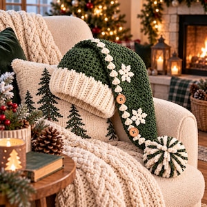 May include: A long, dark green crocheted hat with a thick, cream-colored ribbed brim. The hat features white crocheted snowflake appliques, a decorative trim of small white hearts, two round wooden buttons, and a large, striped pom-pom at the tip.