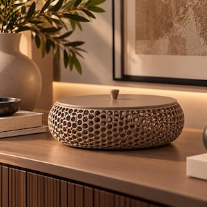 May include: A round, beige storage container with a textured, honeycomb-like lattice exterior and a smooth, flat lid featuring a small, centred knob handle. The container has a low-profile, circular shape and a uniform, neutral colour finish.