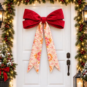 Puede incluir: Un gran lazo decorativo montado en una puerta blanca. La sección superior está hecha de tela roja acolchada, mientras que las dos largas colas colgantes presentan un fondo color crema con un patrón repetitivo de formas florales y geométricas naranjas y rosas.