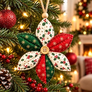 Könnte beinhalten: Ein sternförmiger Weihnachtsanhänger aus Stoff mit sechs gepolsterten Blütenblättern in abwechselnden Farben Rot, Grün und Creme, verziert mit Stechpalmen- und Schneeflockenmustern. Ein kleiner Holzknopf sitzt in der Mitte, befestigt an einer Juteschnur.
