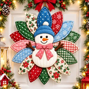 Könnte beinhalten: Ein gesteppter Stoff-Schneemann als Wandbehang mit blauem Hut, orangefarbener Nase und einer rosa gepunkteten Schleife. Der Schneemann ist von einer kreisförmigen Anordnung blütenblattförmiger Stoffstücke mit weihnachtlichen Mustern in Rot, Grün und Blau umgeben.