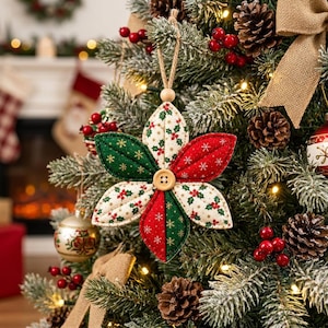 Puede incluir: Un adorno para &aacute;rbol de Navidad de tela con forma de flor de seis p&eacute;talos, con paneles alternos de tela roja, verde y crema con motivos de acebo y copos de nieve. Un bot&oacute;n de madera se sit&uacute;a en el centro y un lazo de yute sirve para colgarlo.