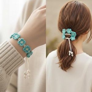 May include: A light blue crochet flower accessory featuring five small blossoms connected by a thin cord. The piece includes two dangling white pearl-like beads at the end of the cord. It is shown worn as a bracelet and as a hair tie.