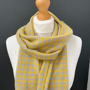May include: A yellow and gray checkered scarf. The scarf is woven with a subtle pattern and is soft and warm.