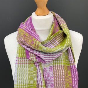 May include: A green and purple plaid scarf with a white background. The scarf is folded and draped around a wooden mannequin.