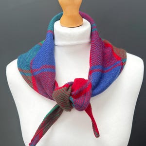 May include: A colorful plaid scarf in shades of blue, red, and green, knotted at the front. The scarf is displayed on a white mannequin, showcasing its vibrant pattern and texture. The scarf is a stylish accessory.