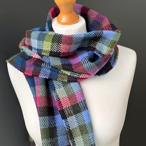 May include: A colorful plaid scarf in shades of blue, pink, green, and black is draped over a mannequin. The scarf is made of a soft, woven material and features a classic plaid pattern. The scarf is a stylish accessory.