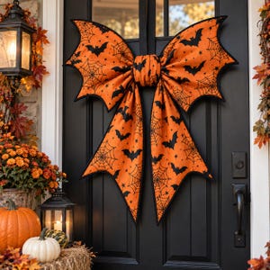 May include: A large orange fabric bow with black bat and spiderweb patterns, featuring pointed wing-like edges. The bow is attached to a black door, serving as a decorative hanging ornament with a distinct Halloween-themed print design.