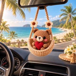 May include: A crocheted brown bear ornament sitting in a small beige basket, holding a red heart. The basket is suspended by two beige ropes adorned with white and brown crocheted flowers, designed to hang from a vehicle rearview mirror.